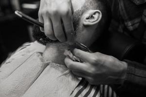 jeune homme barbu se fait raser par un coiffeur au salon de coiffure photo