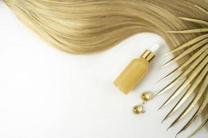 une huile naturelle ou un sérum pour le soin des cheveux et des capsules de traitement dorées sur fond blanc photo