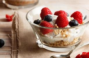 framboises, myrtilles, céréales et yaourt dans un bol en verre sur un sac et des lattes de bois. petit-déjeuner sain pour une vie saine. image horizontale. photo