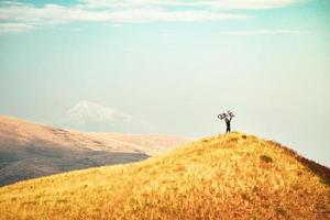 cycliste caucasien ascenseur vélo sur le point de vue supérieur inspiré des montagnes après avoir atteint le sommet. concept de réalisation, d'inspiration, de défi et de détermination photo