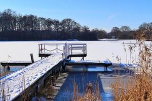 jetée en bois couverte de neige sur un lac gelé par une journée ensoleillée en allemagne. photo