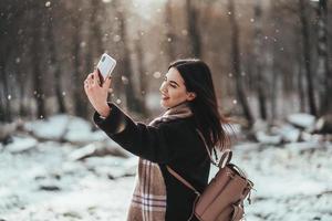 heureuse adolescente souriante ou jeune femme prenant selfie par smartphone dans le parc d'hiver
