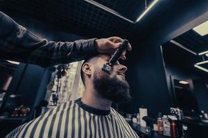 barbier travaille avec une tondeuse à barbe. client hipster se coupe les cheveux. photo