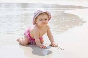 une petite fille souriante joue avec du sable sur la plage près de la mer. développement sensoriel pour les enfants à l'extérieur. photo