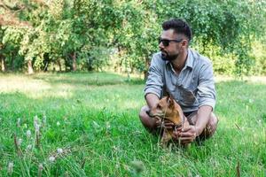 bel homme européen élégant assis sur l'herbe avec son chien dans le parc lors d'une promenade. amitié entre l'homme et les animaux de compagnie. photo