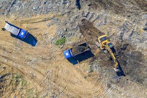 vue aérienne de dessus de l'excavatrice et des camions à benne basculante travaillant sur le chantier de construction photo