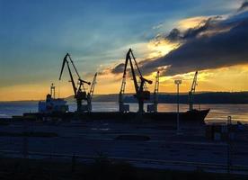 silhouettes de grues et de navires au port au coucher du soleil photo