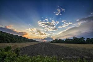 paysage au coucher du soleil du champ rural au crépuscule du soir sous les nuages sur le ciel bleu à la lumière vive du coucher du soleil, vue colorée du champ au crépuscule du coucher du soleil. photo