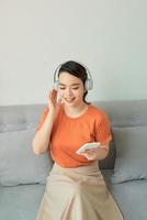 se reposer avec joie. belle jeune femme écoutant de la musique et gardant les yeux fermés assise sur un canapé à la maison photo