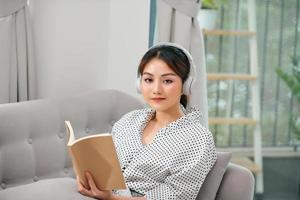 femme avec des écouteurs lisant un livre dans le salon assis sur le canapé photo