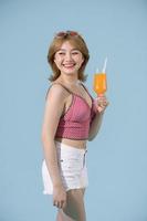 une fille asiatique tient un verre de jus d'orange dans ses bras et sourit en posant en studio photo