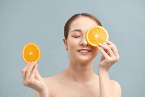 bonne nourriture pour un mode de vie sain. belle jeune femme torse nu tenant un morceau d'orange devant ses yeux en se tenant debout sur fond blanc photo