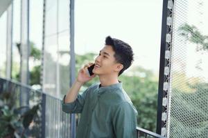 jeune bel homme ayant une conversation sur smartphone au balcon à la journée d'été ensoleillée photo