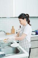 belle jeune femme souriante faisant la vaisselle dans une cuisine blanche moderne. photo