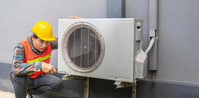 le technicien du climatiseur utilise une clé pour serrer l'écrou du compresseur d'air. réparateur de jeune homme asiatique vérifiant un climatiseur extérieur. photo