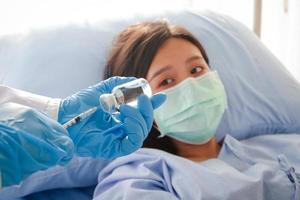 les médecins préparent les vaccinations contre le coronavirus. à un patient, une femme asiatique portant un masque bleu est allongée sur un lit d'hôpital. concept de service médical, assurance maladie photo