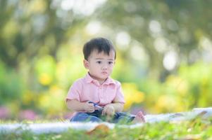 garçon asiatique assis sur le tapis tenant un stylo tout en apprenant de l'extérieur de l'école dans le parc naturel photo