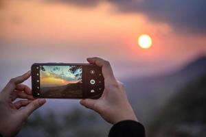 mains de femme tenant un téléphone portable pour prendre une photo au coucher du soleil