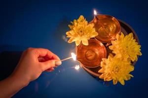 joyeux Diwali. femme allume une lampe à huile traditionnelle. célébrant la fête de la lumière. diya et fleurs jaunes sur fond bleu. photo