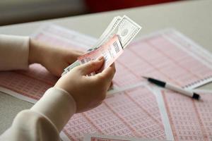 une jeune femme tient le billet de loterie avec une rangée complète de chiffres et de billets d'un dollar sur l'arrière-plan des feuilles vierges de loterie photo