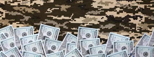 billets d'un dollar américain sur tissu avec texture de camouflage pixélisé militaire ukrainien. tissu avec motif camouflage en formes de pixels gris, marron et vert photo