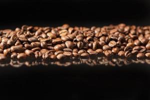 ligne de grains de café torréfiés aromatiques placés sur fond noir.