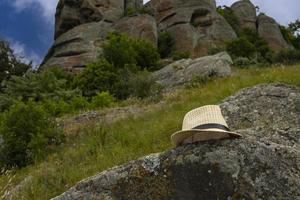 chapeau de soleil d'été en paille, repose sur une grosse pierre sur fond de montagnes rocheuses. photo