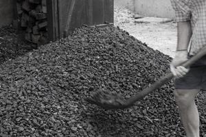 un ouvrier avec une pelle décharge du charbon noir sur fond d'un gros tas de charbon. crise de l'énergie. mise au point douce. photo