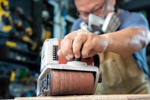 charpentier travaillant avec une ponceuse à bande polissant sur du bois dans un atelier, un fabricant de bricolage et un concept de travail du bois. mise au point sélective photo