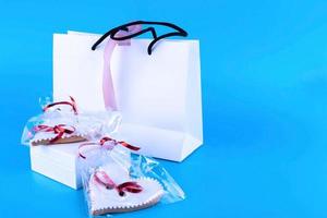 biscuits de la saint-valentin. biscuits sucrés en forme de coeur et sac en papier blanc. cuisson maison. vue d'en-haut. fond bleu. espace de copie. photo