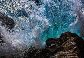 des vagues turquoises d'eau de mer se brisent et vaporisent des gouttes sur des pierres. fermer. mer Rouge photo