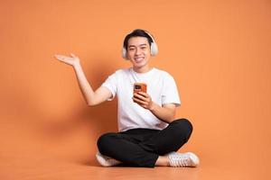 image d'un homme asiatique assis à l'aide d'un téléphone et isolé sur fond orange photo