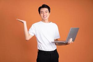 Asian man holding laptop, isolé sur fond orange photo