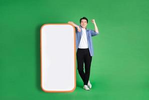 image complète du corps d'un homme asiatique debout à côté d'un grand smartphone, isolé sur fond bleu photo