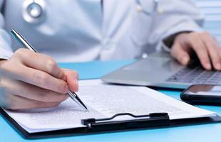 un médecin professionnel signe un document médical de soins de santé de la médecine du patient dans le bureau de l'hôpital. médecin porter un uniforme de blouse de laboratoire lire le dossier du patient sur le bureau pour la personne d'assurance et le stylo de note, espace de copie photo