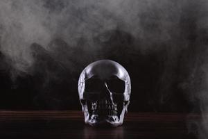 crâne humain halloween sur une vieille table en bois sur fond noir. forme d'os du crâne pour la tête de mort sur le festival d'halloween qui montre l'horreur de la peur des dents maléfiques et effrayant avec de la fumée de brouillard, espace de copie photo