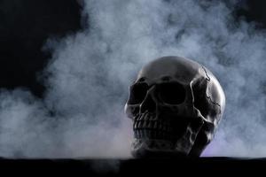 crâne humain halloween sur une vieille table en bois sur fond noir. forme d'os du crâne pour la tête de mort sur le festival d'halloween qui montre l'horreur de la peur des dents maléfiques et effrayant avec de la fumée de brouillard, espace de copie photo