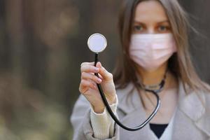 jeune femme portant un masque de protection médicale tenant un stéthoscope pointé vers la mise au point sélective de la caméra. copie espace photo