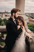 heureuse jeune mariée. la belle mariée et le marié élégant s'étreignent sur le balcon de l'ancienne cathédrale gothique avec vue panoramique sur la ville photo