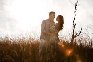 beau jeune couple s'embrassant dans un champ avec de l'herbe au coucher du soleil. homme et femme élégants s'amusant à l'extérieur. concept de journée en famille. espace de copie. photo