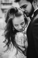 photographie en noir et blanc. heureux couple de jeunes mariés étreignant et embrassant dans la rue de la vieille ville européenne, magnifique mariée en robe de mariée blanche avec beau marié. Jour de mariage photo