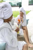 deux jeunes femmes en peignoirs buvant du jus dans le centre de spa. les amis se détendent au spa et au centre de bien-être. parler et boire photo