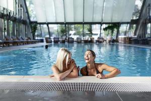 photo de deux femmes qui applaudissent avec des boissons près de la piscine. différents cocktails froids rouges, verts et jaunes avec des glaçons, des pailles, de l'aqua bleu propre et transparent dans la piscine