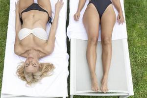 vue de dessus de deux belles jeunes femmes en maillot de bain prenant un bain de soleil au bord de la piscine. photo