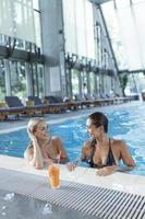 amis au bord de la piscine se détendant en buvant des boissons saines. jeunes femmes sensuelles se relaxant dans la piscine du spa, piscine intérieure du spa photo