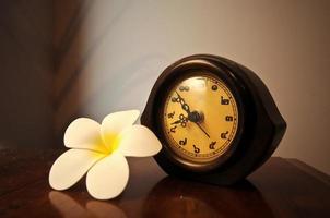 horloge de bureau thaïlandaise en bois vintage sur une table avec fleur de plumeria photo