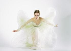 modèle de jeune fille dans un studio photo dans une robe de mariée assise sur un genou jouant avec une robe