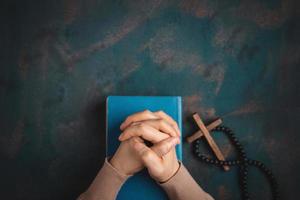 concept de spiritualité, de religion et d'espoir. personne priant par la sainte bible et croix sur le bureau. symbole d'humilité, de supplication, de croyance et de foi pour le peuple chrétien. vue de dessus photo