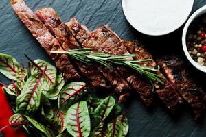 tranches de steak grillé moyen rare servi sur une planche à découper noire avec des légumes photo