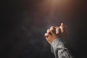 main de personne de prière sur fond noir. une femme catholique chrétienne prie Dieu dans le noir à l'église. fille croit et foi en jésus christ. la religion du christ et le christianisme adorent ou prient le concept. photo